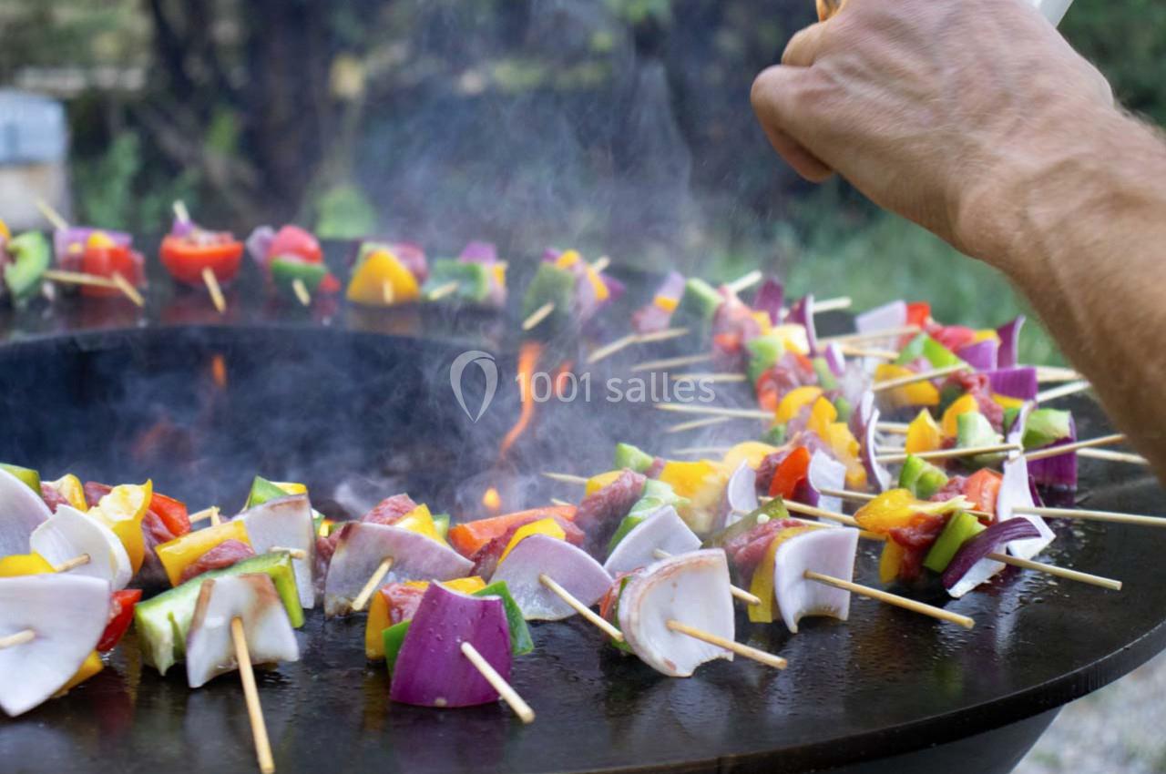 Brochettes de légumes colorés et de viande grillant sur une plancha ronde en plein air.