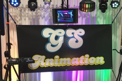 Bannière noire avec le texte ’GS Animation’ suspendue devant un équipement d'éclairage et un écran.