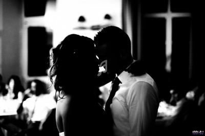 Un couple dansant en contre-jour dans une salle éclairée, entouré de silhouettes floues en arrière-plan.