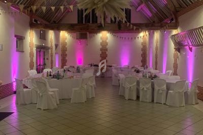 Salle de réception avec poutres apparentes, tables décorées et éclairage rose tamisé.