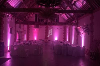 Salle de réception avec poutres apparentes, éclairage rose et tables dressées pour un événement.