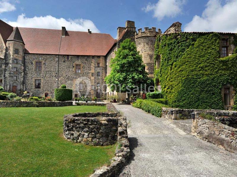 Cour intérieure d'un château en pierre avec murs recouverts de lierre, pelouse entretenue et allée gravillonnée.