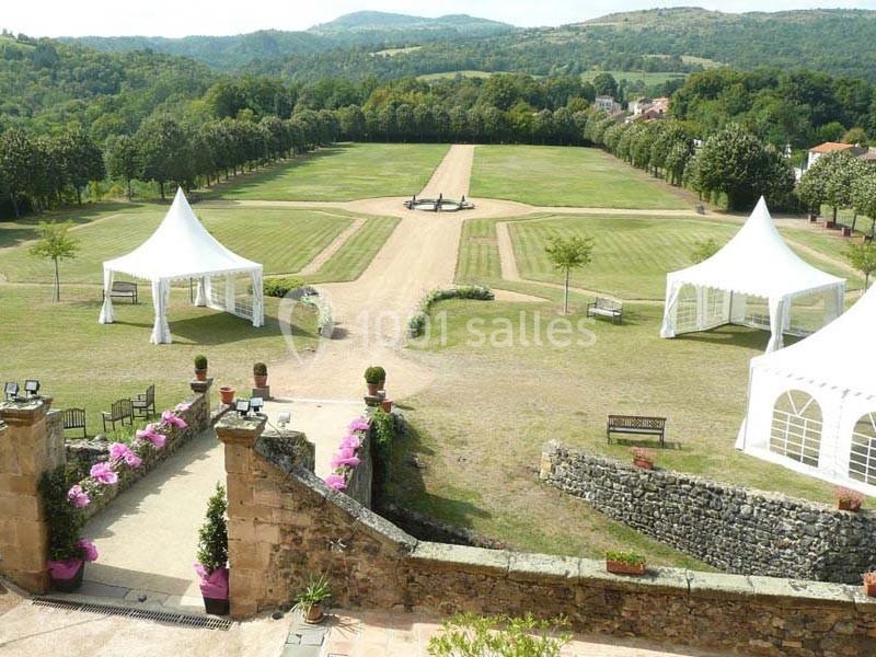 Vue d'un grand jardin avec allées gravillonnées, pelouses, tentes blanches et collines verdoyantes en arrière-plan.