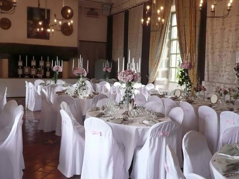 Salle de réception élégamment décorée avec des tables rondes, nappes blanches, chandeliers et compositions florales.