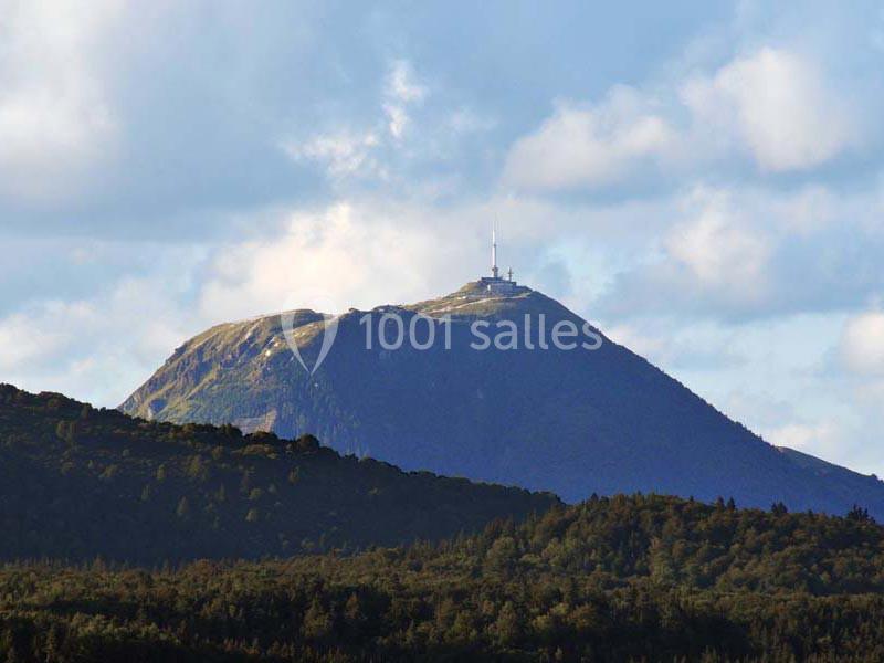 Vue d'un sommet montagneux avec une antenne et un bâtiment au sommet, entouré de forêts et sous un ciel partiellement…