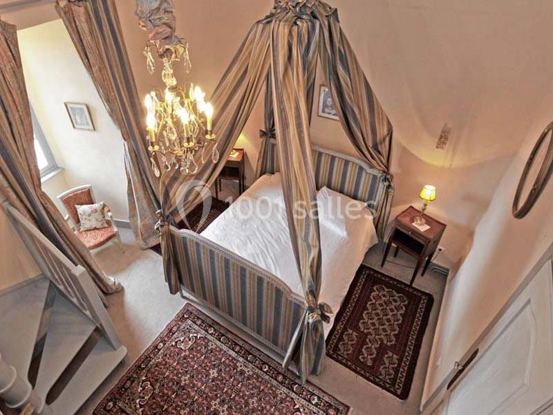 Lit à baldaquin avec draperies rayées dans une chambre chaleureuse, éclairée par un lustre et des lampes de chevet.