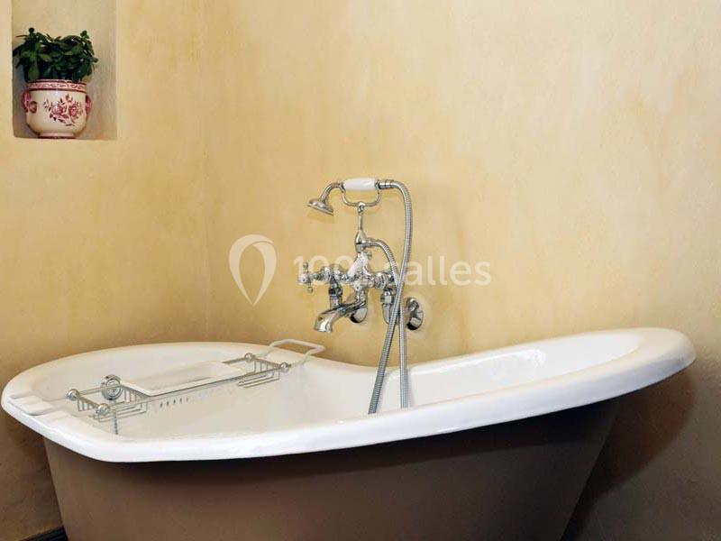 Baignoire blanche sur pied avec robinetterie chromée et mur beige en arrière-plan.