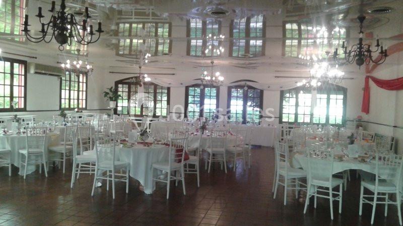 Salle de réception lumineuse avec des tables rondes dressées, des chaises blanches et des lustres suspendus.