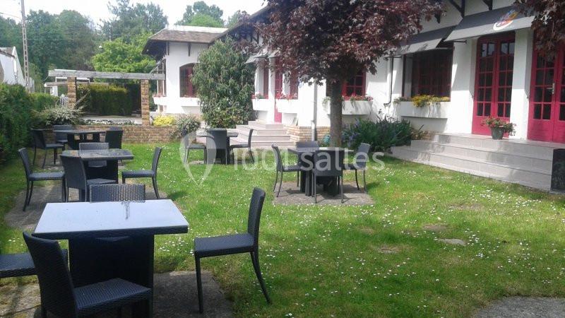 Tables et chaises noires disposées sur une pelouse devant un bâtiment blanc avec des fenêtres rouges.