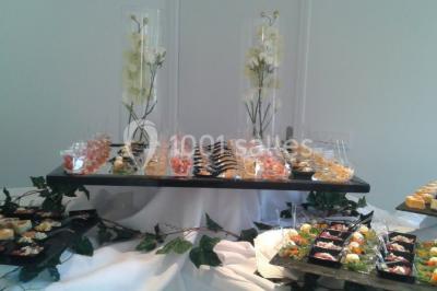 Buffet élégant avec verrines colorées, petits plats variés et décoration florale blanche sur nappes blanches.