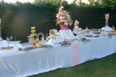 Buffet élégant avec verrines colorées, petits plats variés et décoration florale blanche sur nappes blanches.