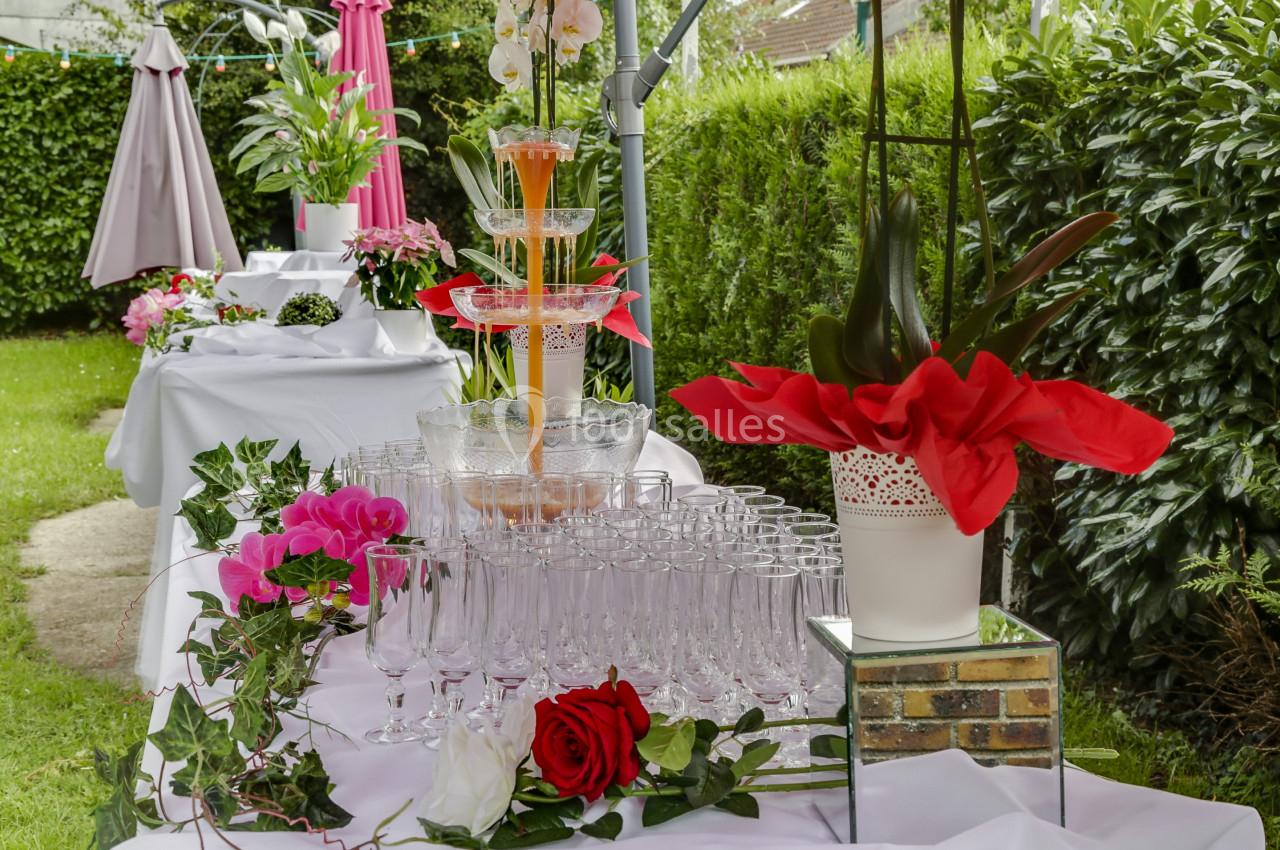 Fontaine à cocktails entourée de verres et de décorations florales sur une table dressée dans un jardin.