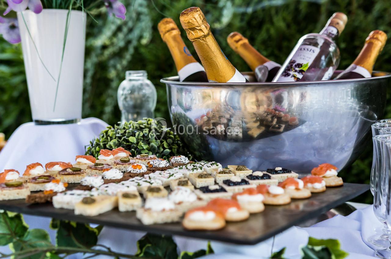Plateau de canapés variés devant un seau rempli de bouteilles de champagne et de vin, décoré de verdure.