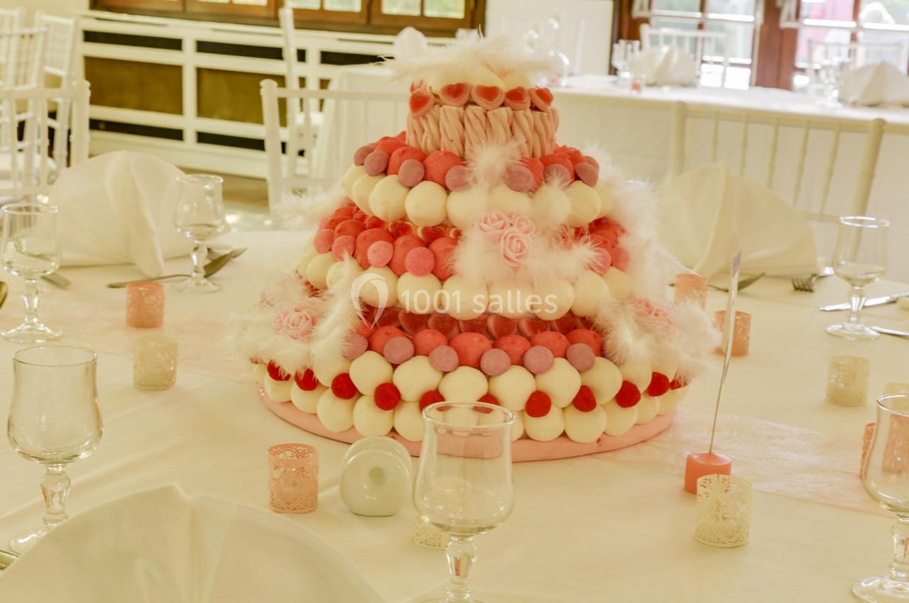 Pièce montée décorative en bonbons roses et blancs, disposée sur une table dressée avec des verres et des bougies.