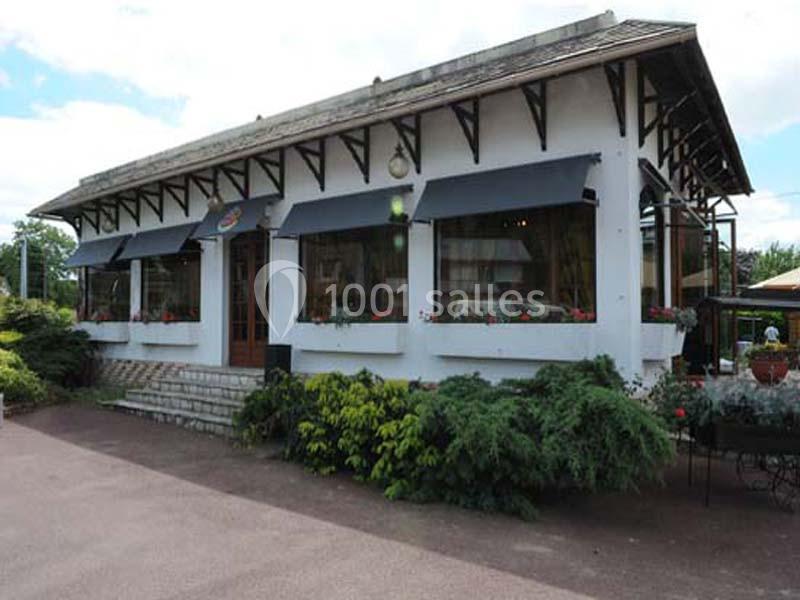 Façade d'un bâtiment blanc avec des auvents noirs, entouré de végétation et situé sur une allée pavée.