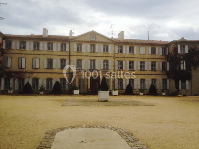 Façade d'un grand bâtiment ancien à trois étages avec des volets, entouré d'une cour en gravier.