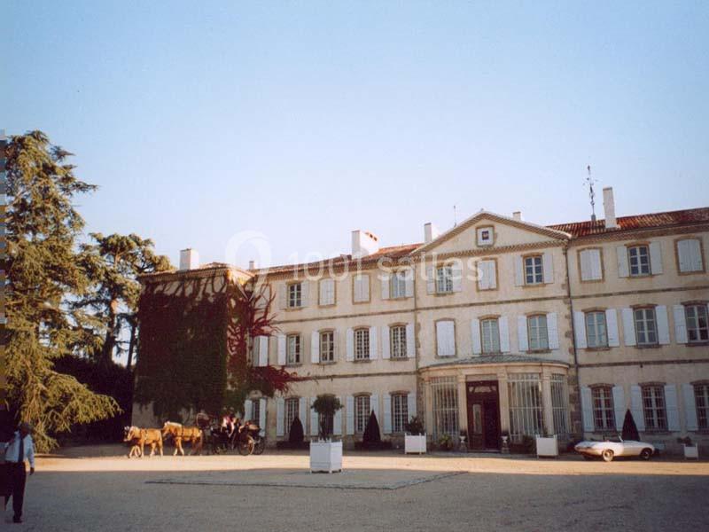 Façade d'un grand bâtiment ancien avec des volets blancs, une vigne grimpante et une calèche devant l'entrée.