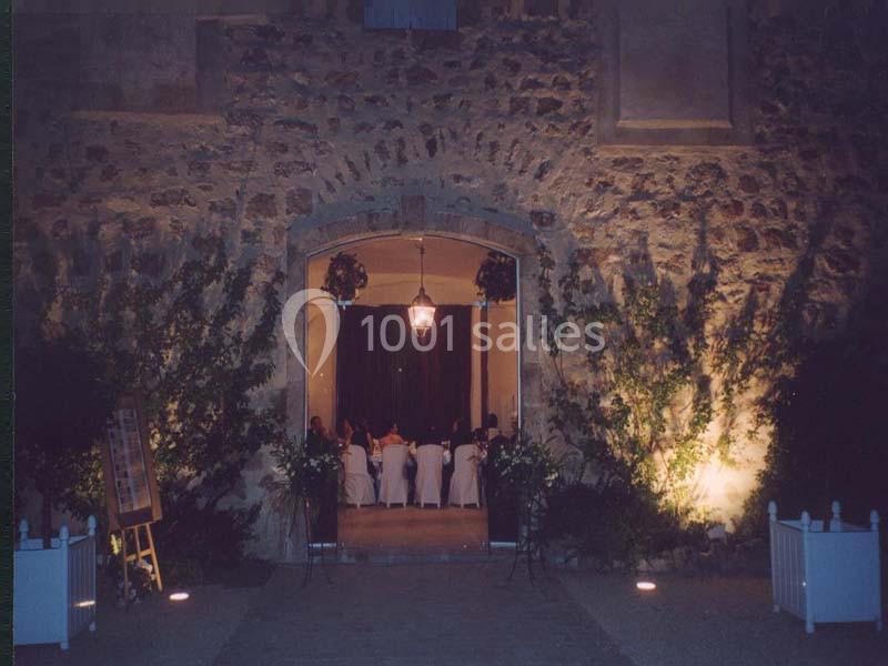 Entrée voûtée en pierre éclairée, donnant sur une salle où des convives sont assis autour d'une table.