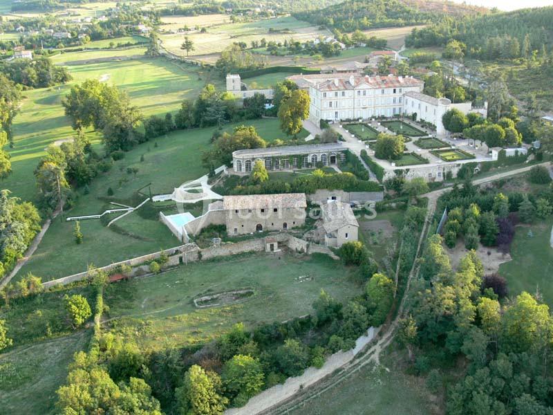 Vue aérienne d'un domaine historique avec bâtiments en pierre, jardins aménagés et paysage verdoyant environnant.