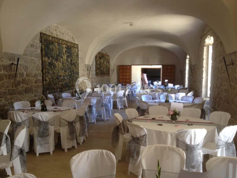 Salle voûtée en pierre aménagée pour un événement, avec tables rondes dressées et chaises couvertes de housses blanches.