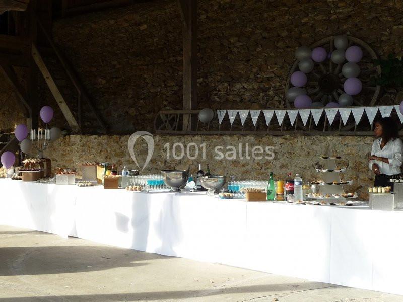Table de buffet décorée pour un événement, avec desserts, boissons et guirlandes dans un espace extérieur en pierre.