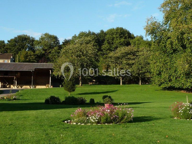 Pelouse verdoyante avec parterres de fleurs, arbres en arrière-plan et bâtiment rural sur la gauche.