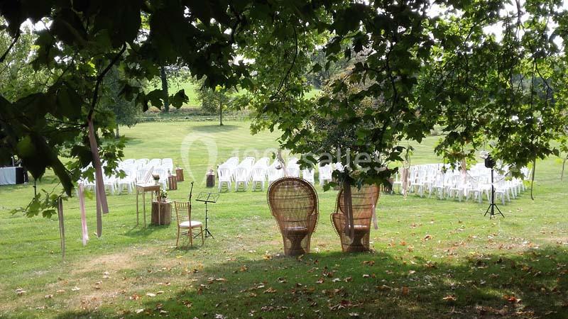 Chaises blanches disposées en extérieur sur une pelouse, entourées d'arbres, avec des fauteuils en osier au premier plan.