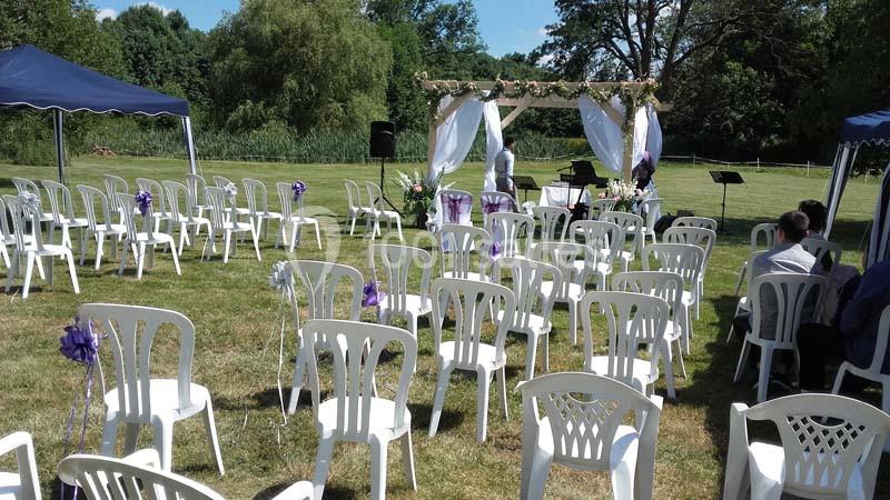 Chaises blanches disposées en rangées devant une arche décorée pour une cérémonie en plein air dans un jardin.