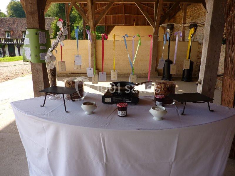 Table dressée avec des ustensiles de cuisine, pots de confiture et décorations colorées dans un espace couvert en bois.