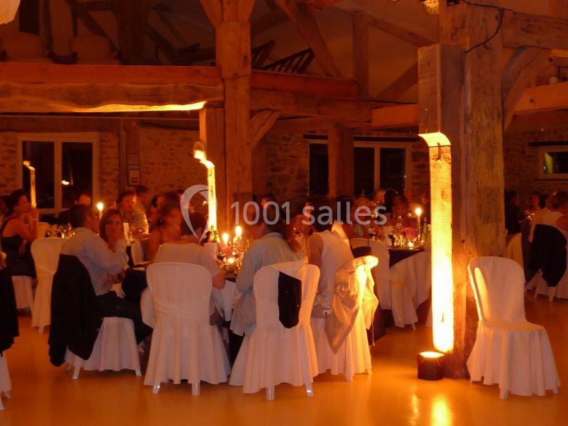 Des convives assis à des tables éclairées par des bougies dans une grande salle avec poutres apparentes.