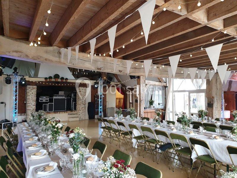 Salle de réception décorée avec des guirlandes, des tables dressées et des fleurs, prête pour un événement festif.