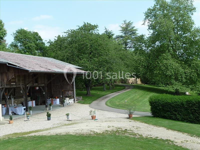 Grange en bois avec tables dressées à l'extérieur, entourée de pelouse, arbres et chemin sinueux.