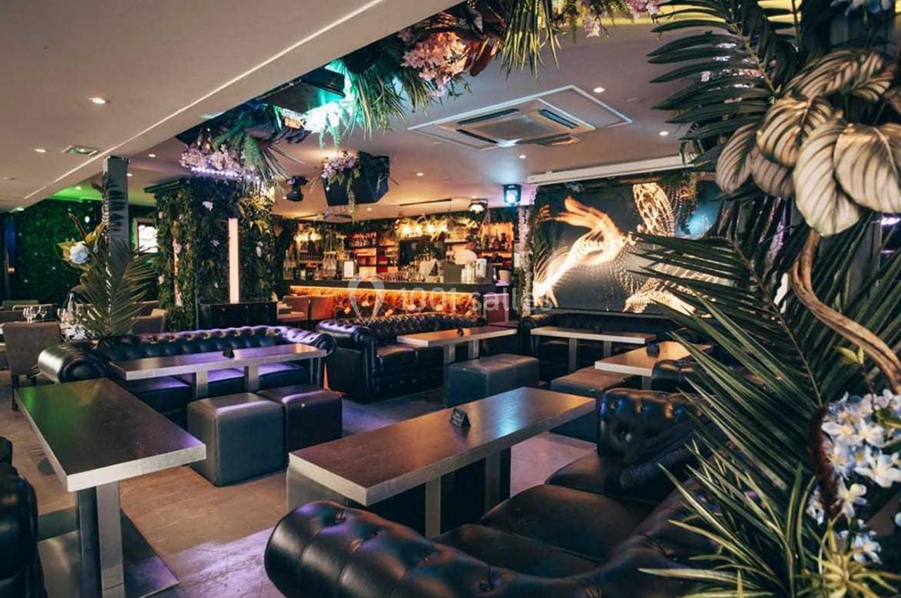 Intérieur d'un bar lounge avec canapés en cuir, tables basses, décorations végétales et éclairage tamisé.