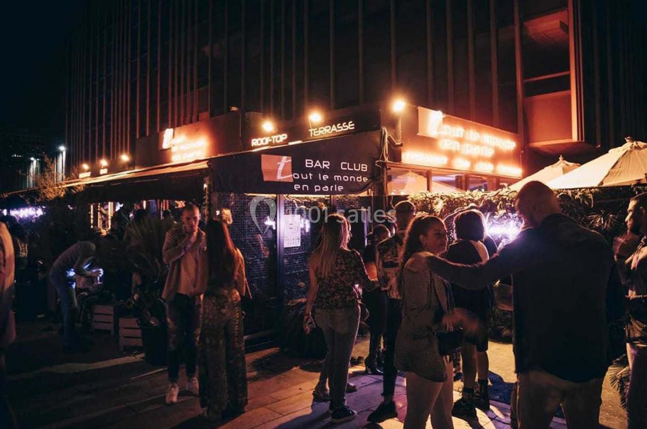 Groupe de personnes discutant et se détendant sur la terrasse éclairée d'un bar en soirée.