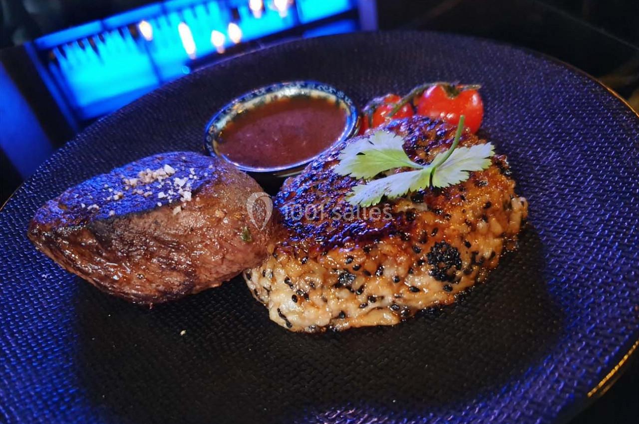 Assiette avec un steak, un accompagnement de riz grillé garni de coriandre, une sauce et des tomates cerises.