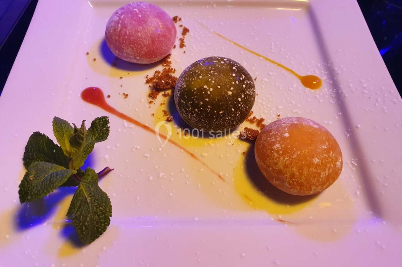 Trois mochis colorés sur une assiette blanche, décorés de coulis, miettes et feuilles de menthe.