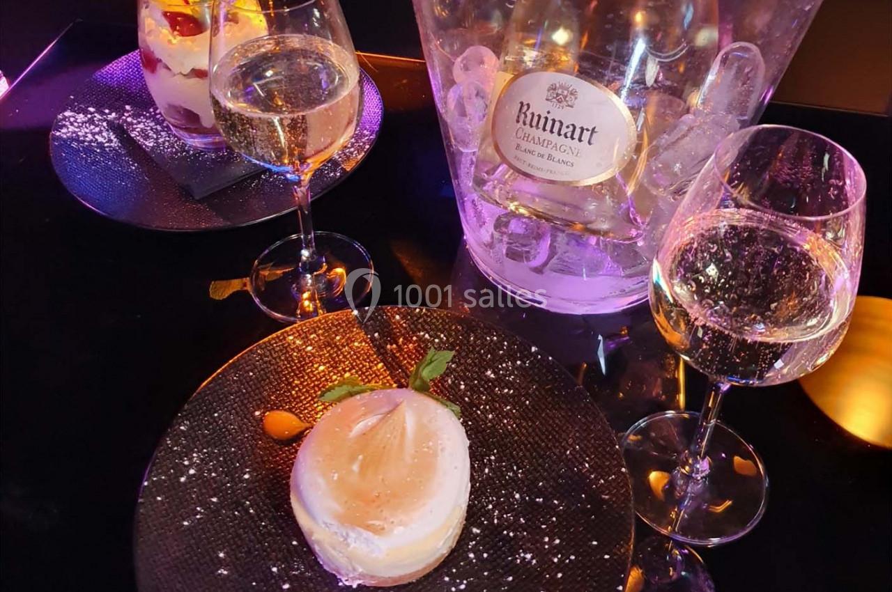 Deux verres de champagne, un dessert sur assiette noire et un seau à glace contenant une bouteille de Ruinart.