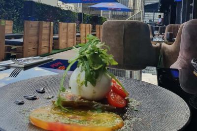 Planche de charcuterie et fromages sur une table en terrasse, avec une bouteille de vin blanc dans un seau à glace.