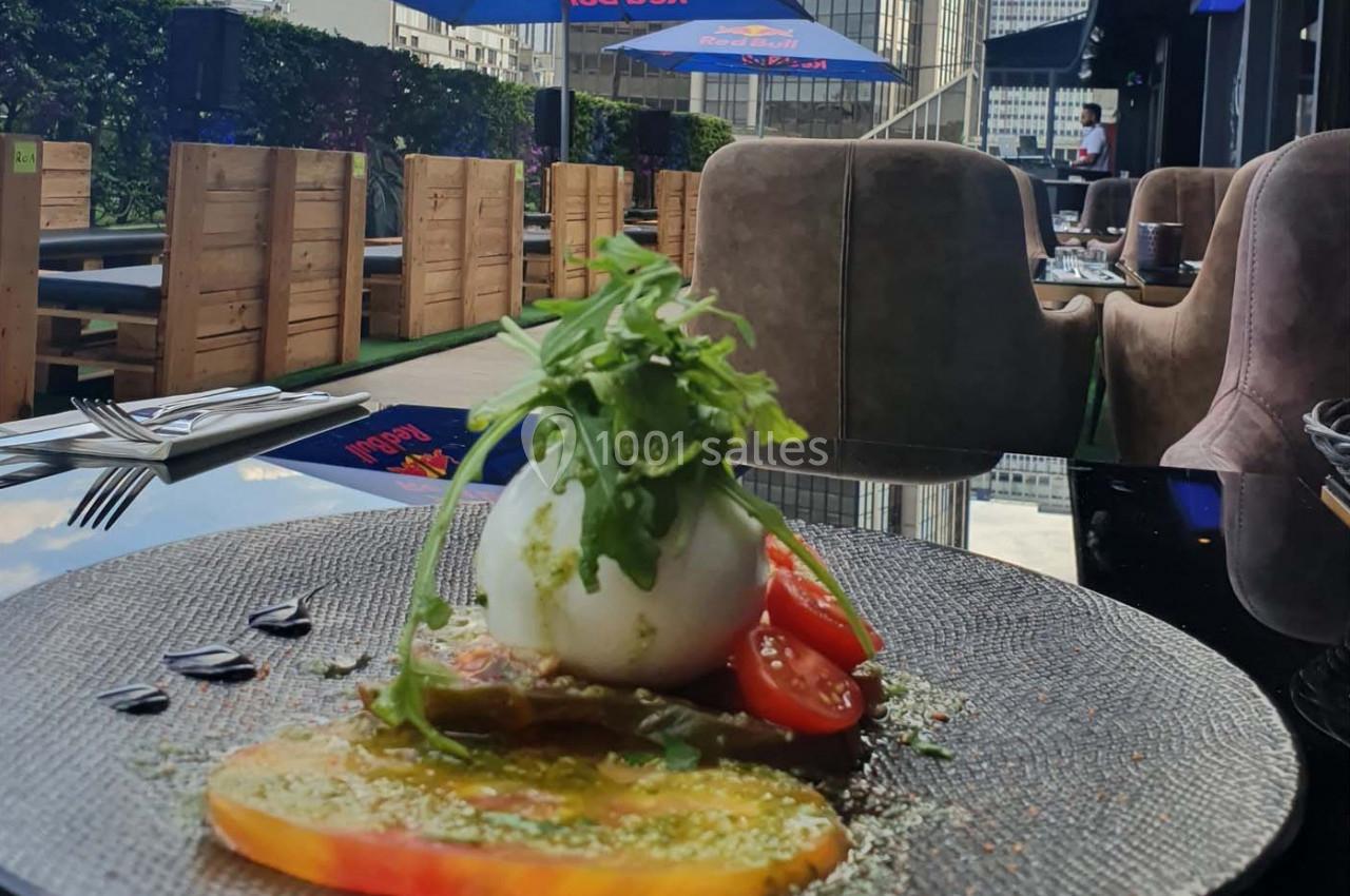 Assiette de burrata garnie de roquette, tomates colorées et assaisonnement, servie en terrasse avec mobilier en bois.