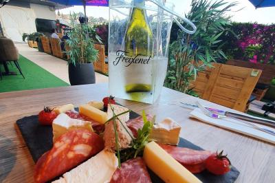 Planche de charcuterie et fromages sur une table en terrasse, avec une bouteille de vin blanc dans un seau à glace.