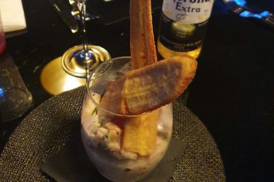 Assiette de viande garnie de roquette et sauce rouge, servie sur une table avec des verres de vin en arrière-plan.