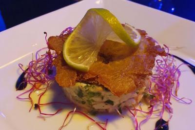 Assiette de viande garnie de roquette et sauce rouge, servie sur une table avec des verres de vin en arrière-plan.