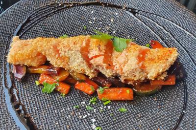 Assiette de viande garnie de roquette et sauce rouge, servie sur une table avec des verres de vin en arrière-plan.