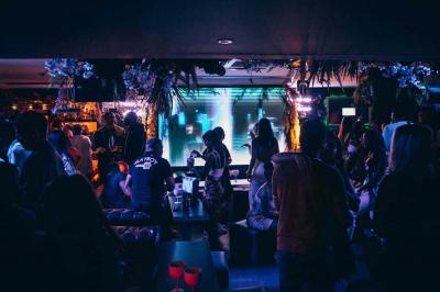 Assiette de viande garnie de roquette et sauce rouge, servie sur une table avec des verres de vin en arrière-plan.