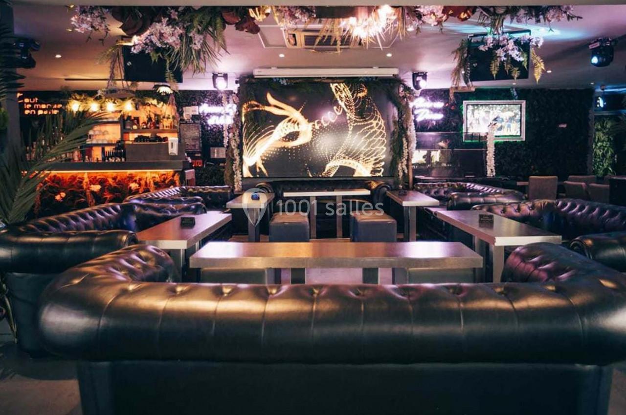 Intérieur d'un bar avec canapés en cuir noir, tables basses, éclairage tamisé et décoration murale lumineuse.