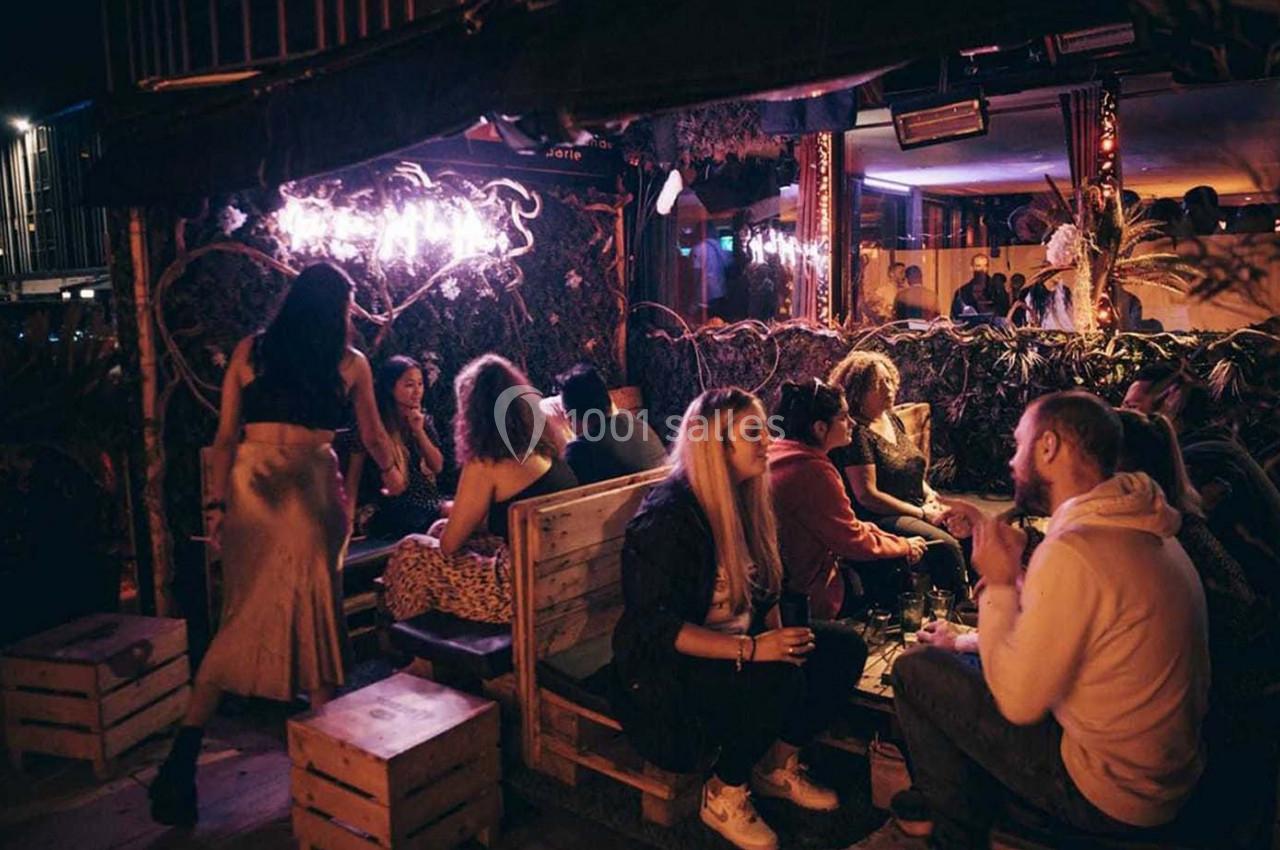 Des personnes discutent et partagent un moment convivial dans un bar à l'ambiance tamisée et décor végétal.