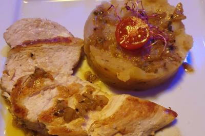Assiette de viande garnie de roquette et sauce rouge, servie sur une table avec des verres de vin en arrière-plan.