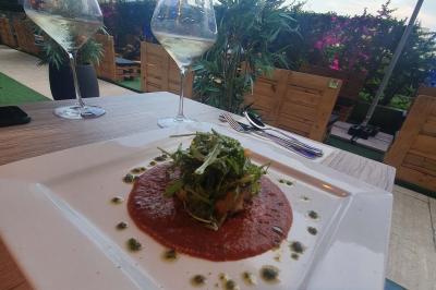 Assiette de viande garnie de roquette et sauce rouge, servie sur une table avec des verres de vin en arrière-plan.