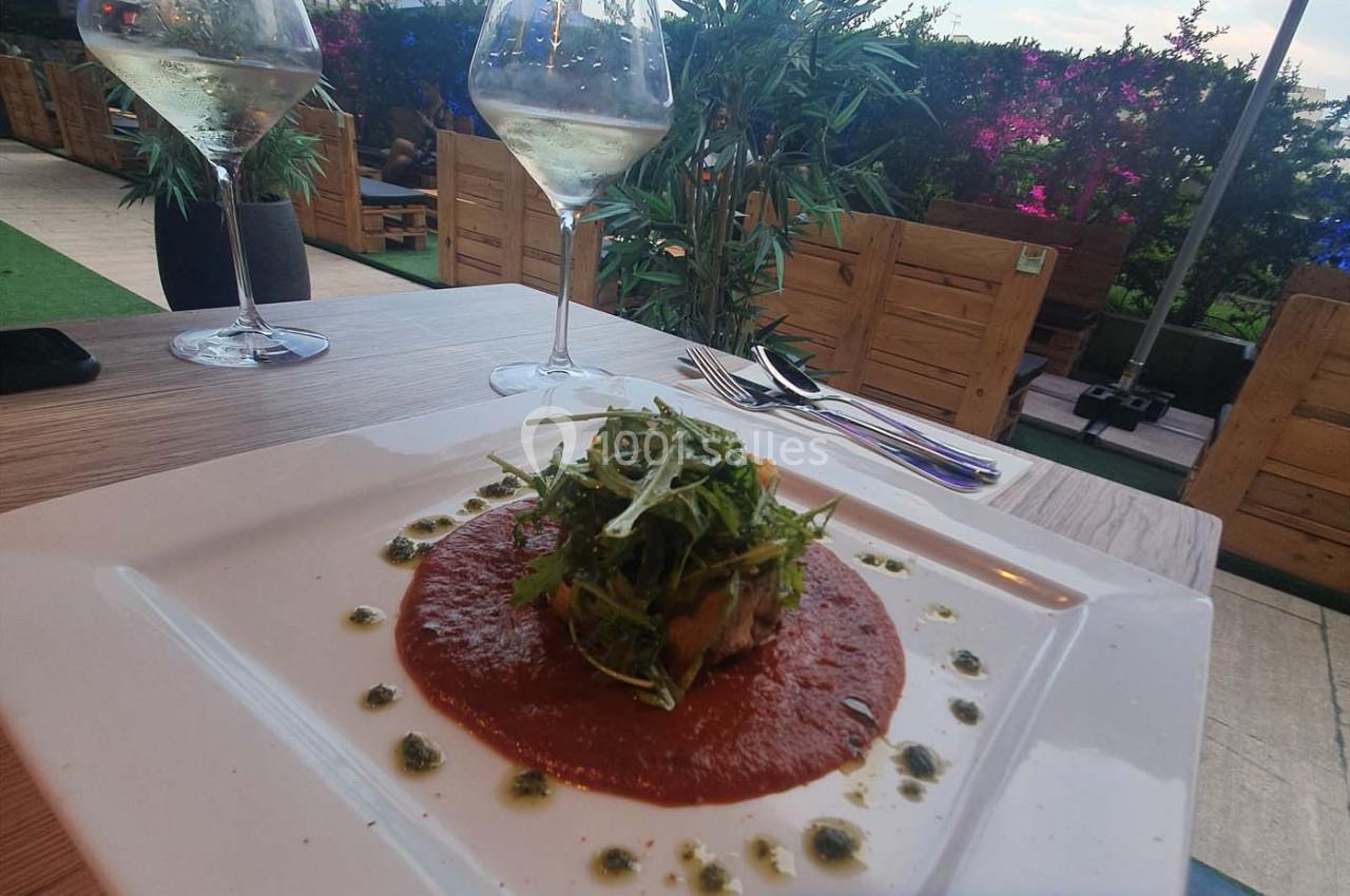 Assiette de plat dressée avec une garniture de roquette sur une sauce rouge, entourée de touches de sauce verte.