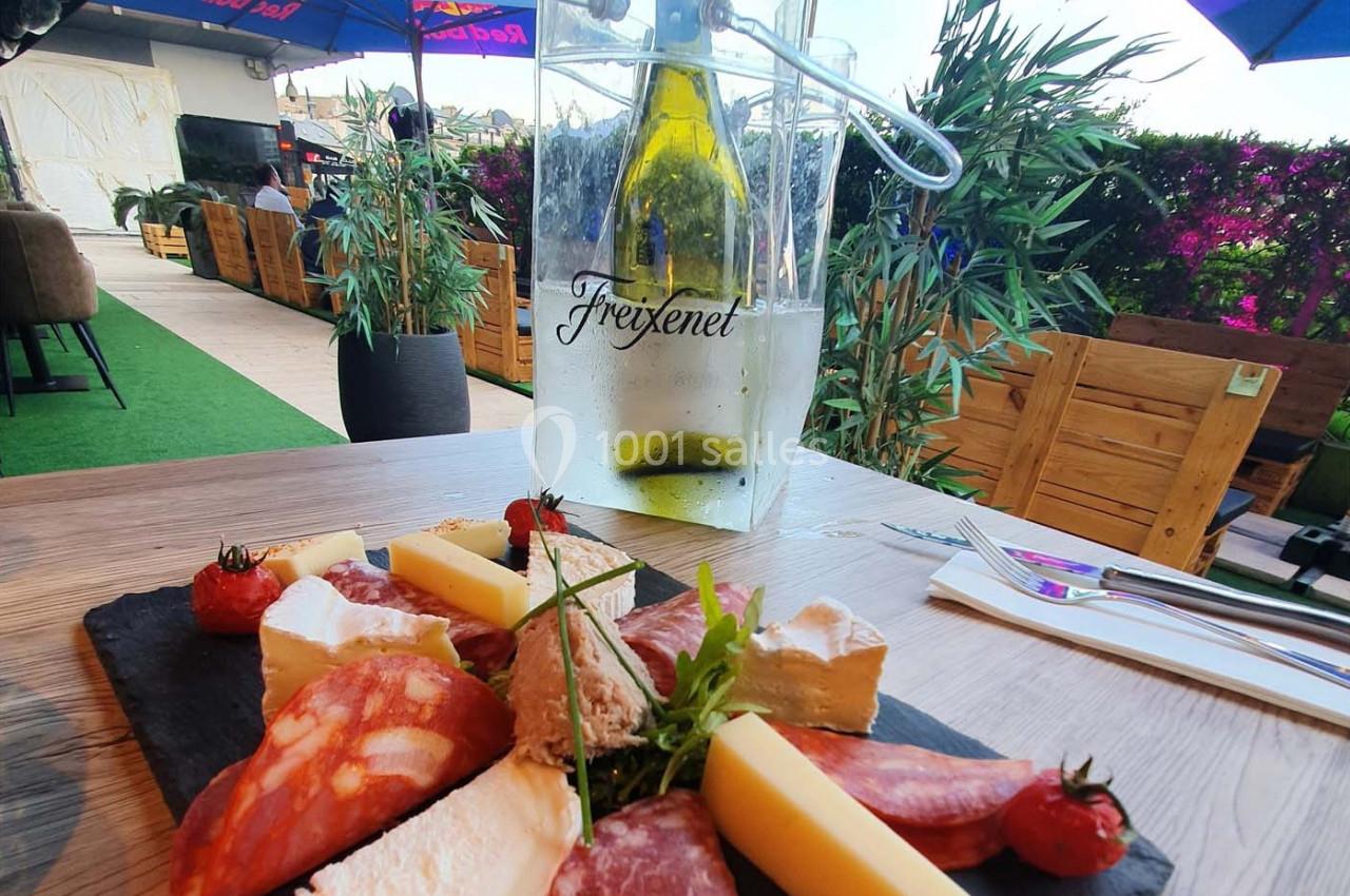 Plateau de charcuterie et fromages sur une table en terrasse, avec une bouteille de vin blanc dans un seau à glace.
